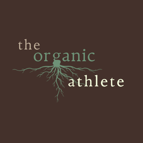 A logo for "The Organic Athlete" featuring earthy tones. The background is a deep brown color. The text "the" and "athlete" are in a light beige font, while "organic" is in a muted green. Below "organic," there is a stylized root system extending downward, symbolizing natural growth, strength, and connection to the earth. The font style is simple yet organic, aligning with a natural and holistic theme.